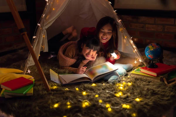 アジアの母と娘は 彼らのベッドルームでテントと光でリラックスし 自宅で夜にタブレットトークアップを読みます — ストック写真