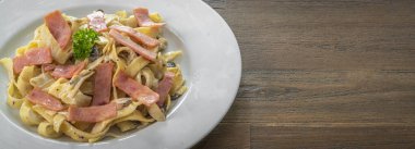 Beyaz tabakta jambonlu mantar soslu spagetti İtalyan restoranındaki ağaçlık masaya.