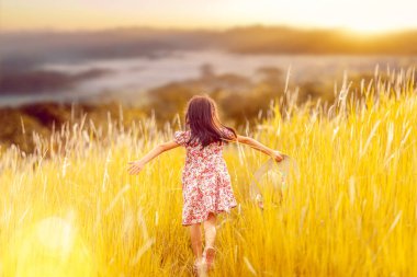 Asyalı kız yeşil çayırlarda oynuyor ve eğleniyor çimenlerde koşuyor, giyinmiş çocuk ve gün batımlı doğa. 