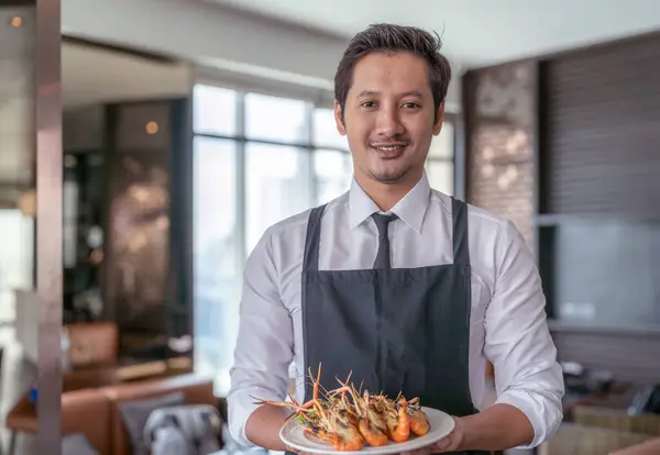 Asian man waiter working and carry and serve dish of sea food in luxury restaurant