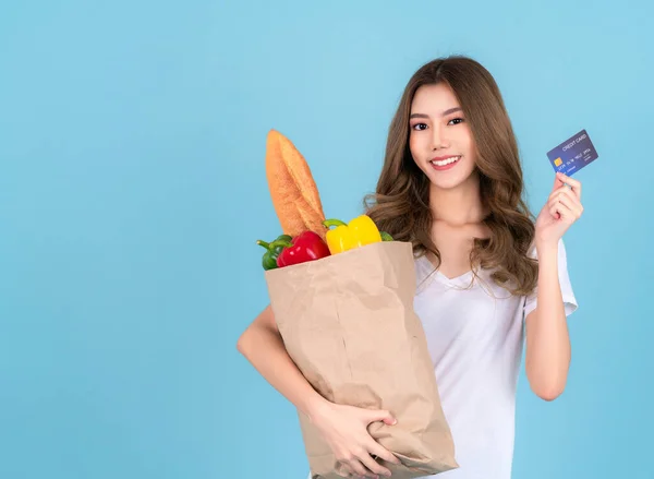 Asian woman carry paper shopping bag from supermarket with  vegetables inside a bag and pay money by credit card with isolated background