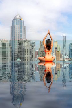 Asyalı gezgin kadın Bangkok, Tayland manzaralı otelin çatısındaki yüzme havuzunda yoga postasında uyuyor ve dinleniyor.