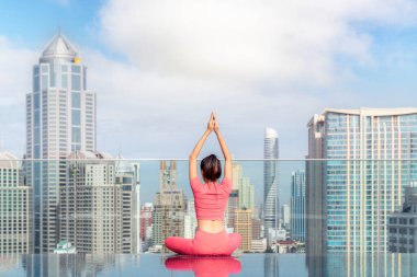 Asyalı kadın, Bangkok şehri çatısı ve yüzme havuzu geçmişi olan, Pilatus hareketi için temel poz veren bir yoga hareketi sergiliyor.