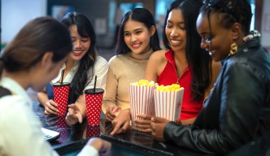 Asyalı bir kadının mutlu arkadaş grubu sakin olun ve Cimema sinemasına birlikte gidin ve bilet ve satış reyonunda patlamış mısır alın.