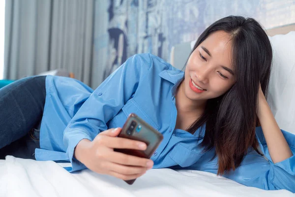 Asian traveller woman take travel bag sleep on the bed and check masage in her mobile in her hotel room after finish her travel trip