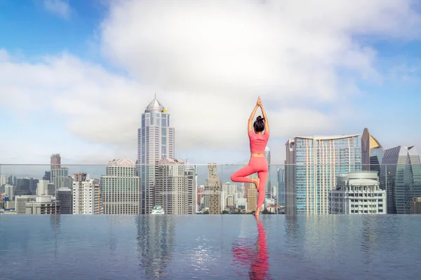 Asian woman pose yoga action on hotel rooftop with Bangkok city and swimming pool background, basic pose for Pilate action