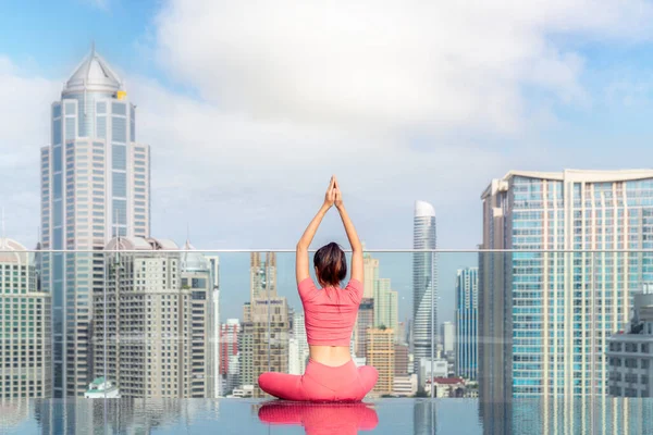 Asian woman pose yoga action on hotel rooftop with Bangkok city and swimming pool background, basic pose for Pilate action