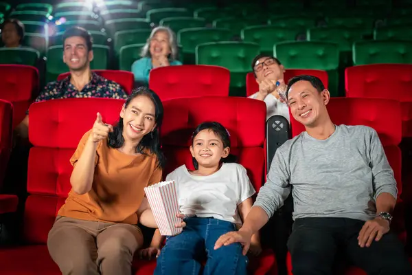 アジアの家族の幸せな旅行は赤い座席に座って映画館で楽しんで 人々は週末にリラックスして休日のアクティビティ ストックフォト