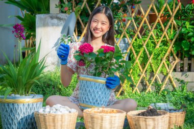 Asyalı kadın bahçıvan bahçesinde çiçek saksısı ve yeşil arka planda bahçıvan malzemesi ile rahatlar.
