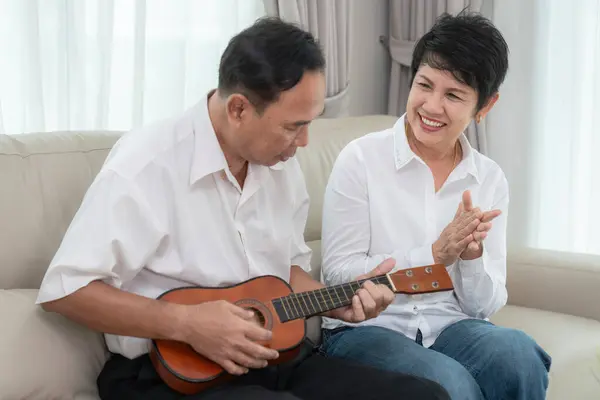 Asian okd couple sing a song with happy emotional and play ukulele togather in living room at they home