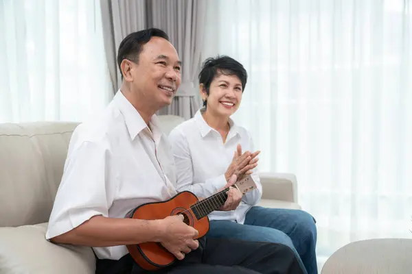 Asian old couple sing a song with happy emotional and play ukulele togather in living room at they home