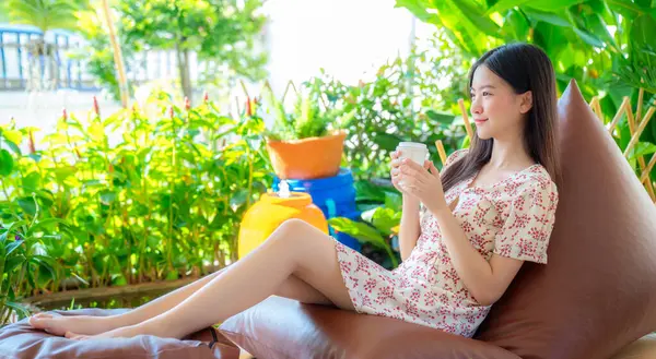 アジアの女性は 自宅の庭 リゾートの緑の自然で手でコーヒーカップで眠り リラックス ロイヤリティフリーのストック画像