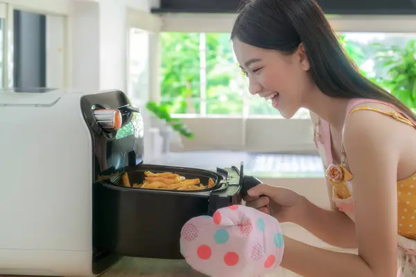 亚洲妻子在家里的厨房里用电炉煮土豆 无油薯条 图库图片