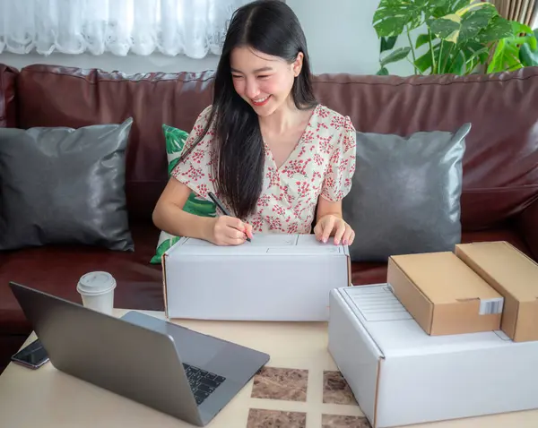 ホームオフィスで働くアジアのビジネス女性と自宅のオフィスでオンラインショッピングアプリで製品を配信 ストックフォト
