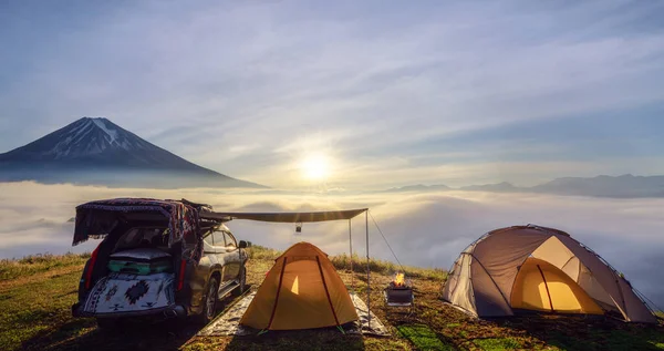 山頂のオレンジテントとキャンプは霧の海と山の頂上を目の前にした 日の出の時間とテントと一緒に旅行するための車があります ロイヤリティフリーのストック画像
