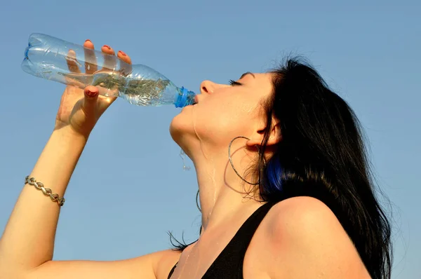 stock image young attractive woman drinks cold water in hot day on blue sky background