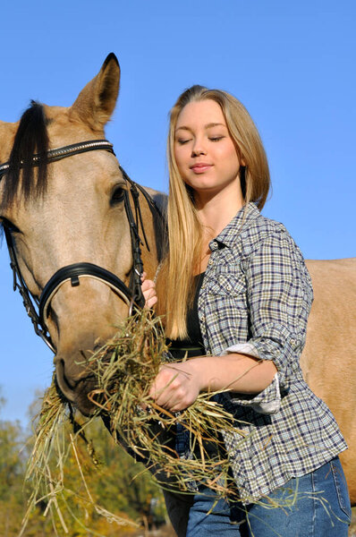 teenage girl feeding horse in sunny autumn day 
