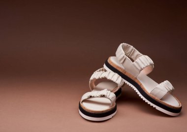 Üç renkli tabanlı modern pastel deri sandaletler birbirinin üzerine yerleştirilmiş. Kopyalama alanı olan kahverengi arkaplan. Ayakkabı satma kavramı