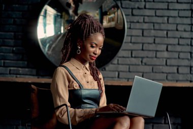 Modern bir ofiste oturan ve dizüstü bilgisayarda yazan çekici siyahi kadın. Genç girişimci iş yapıyor. Uzaktan çalışan kadın danışman, online yönetim kariyeri ve sanal ağ işi