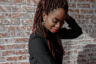 Kusursuz ciltli, sarı saçlı, şık makyajlı, siyah gömlekli ve dokunaklı küpeli güzel Afrikalı bir kadının portresi..