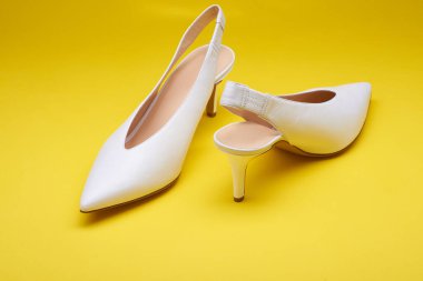 Şık, beyaz kadın deri, yüksek topuklu, arka bağcıklı, parlak sarı arka planda izole ayakkabılar. Yakın çekim görüntüsü. Modaya uygun kadın ayakkabıları, gelin ayakkabıları.