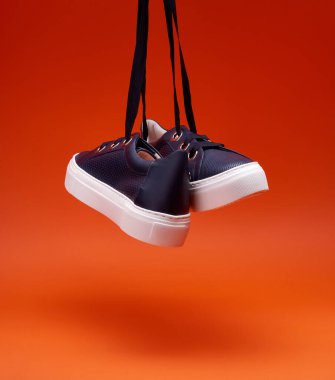 Modern lacivert ayakkabılar parlak turuncu arka planda asılı duruyor. Delinmiş deri, kalın beyaz taban, geniş ayakkabı bağcığı, metal göz bilekleri. Sıradan ayakkabılar, spor ayakkabılar. Ayakkabı reklamı konsepti.