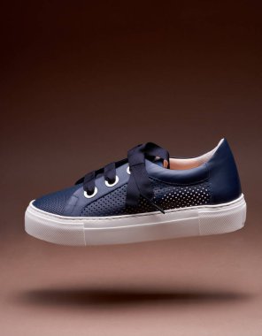 Kalın kahverengi arka planda kalın ayakkabı bağcıkları olan delinmiş deriden mavi kadın spor ayakkabısı konsepti. Sıradan tarz kadın ayakkabıları..