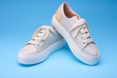 Mavi arka plandaki modern spor ayakkabılarına yakından bakın. Arkasında bej rengi deri, pastel ve sarı detaylar var. Şehir tarzı ayakkabı konsepti.