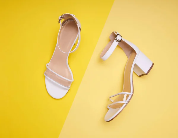 Fashionable open-toe white women\'s sandals with block heels, clear vamps, ankle straps and beige insoles, isolated on a yellow background. Fashion photography