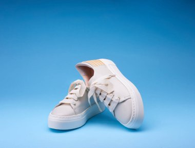 Pastel bej bir çift spor ayakkabı, şık ayakkabı bağcıkları ve bac ile ilgili ilginç detaylar. Kademe mavi arka plan. Ayakkabı satmak için yaratıcı tasarım