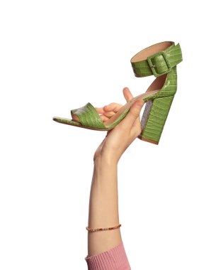 Beyaz arka planda izole edilmiş yeşil topuklu sürüngen deri bir ayakkabı tutan bir kadın eli. Elinde şık bir ayakkabı sunumu