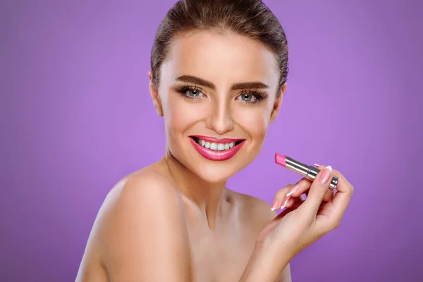 コピースペースのある紫色の背景に対して光沢のあるピンクの口紅を塗る魅力的な笑顔の女性 化粧品 化粧品 美容業界向けのレイアウト デートの準備をする少女 — ストック写真