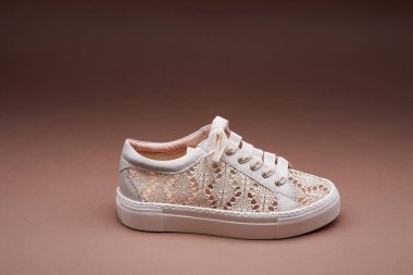 Beyaz, kalın kauçuk tabanlı, kahverengi arka planda bej rengi, örülmüş bir spor ayakkabı. Modern ayakkabı konsepti