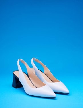 Beyaz, sivri uçlu kadın ayakkabıları, açık bir sırt ve siyah işaret topuklu topuklar, fotokopi alanı olan mavi bir arka plan. Ayakkabı ile yaratıcı minimalist yerleşim.