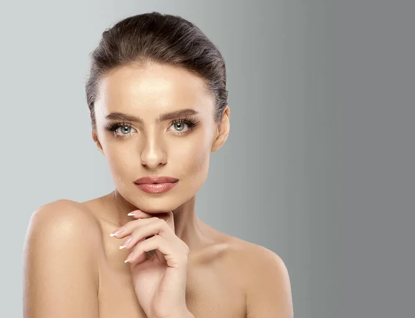 stock image Skin care. Attractive woman with bare shoulders, expressive gray eyes, long eyelashes, full lips, and smooth skin holds her hand under her chin isolated on a gradient gray background. Beauty concept.