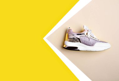 Fotokopi makinesini işaret eden sarı-beyaz-bej arka planda izole edilmiş beyaz tabanlı, metal ve saten ayakkabı bağcıklı şık, parlak spor ayakkabılar. Yan görüş. Moda günlüğü.