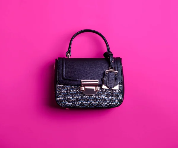 Stylish woman's top-handle bag made of  black leather and multicolored textile, with metal clasp and tag isolated against a magenta background. Mock-up for online fashion store or blog.