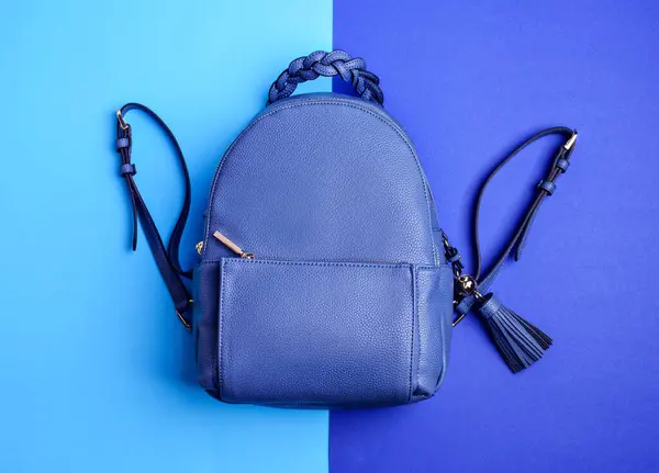 Modern royal blue leather backpack with zipped pocket with an original braided handle and a tassel isolated on a two-toned blue background. Creative design for advertising poster. Fashion blog.