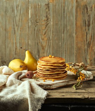 Tahtaya yerleştirilmiş pofuduk tereyağlı krep resmi. İki armut ince bir zemin hazırlarken, yanlarında bir deniz dikeni ve bir bal kaşığı duruyor. Gıda Dergisi Düzeni.