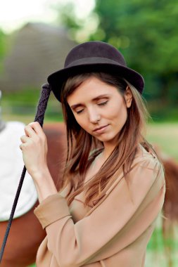 Bir portrede gözlerini kapalı tutarken arka plandaki atın yanında dingin genç bir kadın. Sağlık, sakinlik konsepti. Çiftlikteki kapalı bir çayırda bir atla poz vermek.