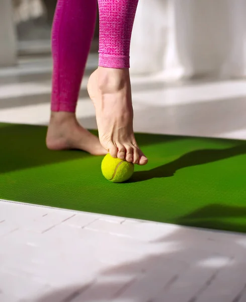 Tennis ball roll massage for feet. Woman practicing foot self-massage with a tennis ball. Physiotherapy, reflexology. Tension relieving in the plantar fascia. Improving foot joint mobility.