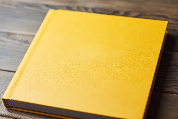 Stylish book with yellow leather hardcover isolated on a wooden background. Perspective view, closeup. Photobook, photo album, diary, planner or scrapbook. Template for photographers or designers.