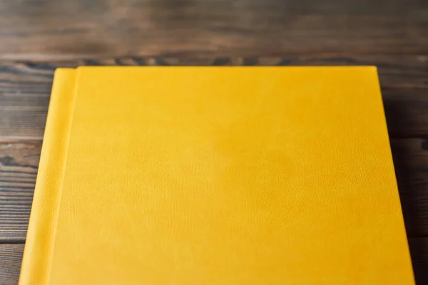 Book with yellow textured hardcover isolated on a brown wooden background. Perspective view, close-up, cropped. Layout with blank cover. Concept of reading or studying.