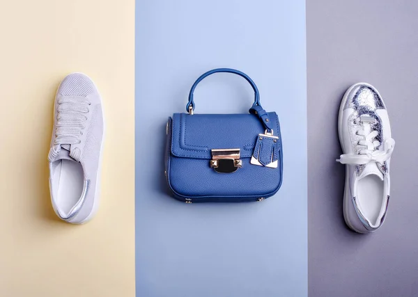 Trendy royal blue leather top-handle bag and two different shoes: white-silver sneaker with a cracked effect and pastel perforated leather sneaker on a two-tone background. Fashion blogger content.