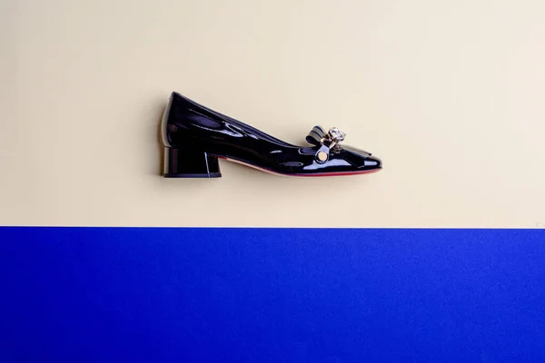 Chic female black patent leather shoe with low flare heel and front embellishment on a contrasting two-color background with copy space. Elegant footwear concept. E-commerce, discounts, season sales.