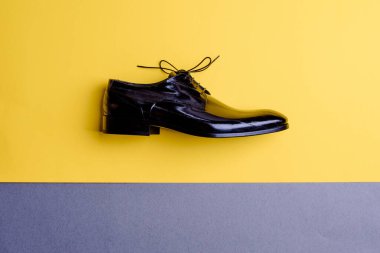 Fotokopi alanı olan sarı-gri kontrast bir arka planda izole edilmiş siyah deri erkek ayakkabısı. Üst manzara, düz yatış. Resmi erkek aksesuarları. Bahar ayakkabı satışı kampanyası, outlet pazarlama