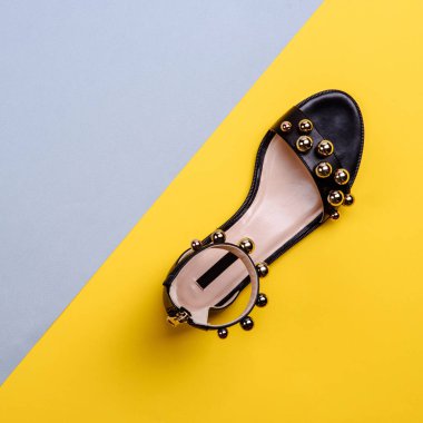 Fotokopi alanı olan yaratıcı mavi-sarı arka planda büyük altın boncuklarla süslenmiş bej tabanlı siyah deri bileklikli kadın sandaleti. Ayakkabı mağazası reklamı için bir model..