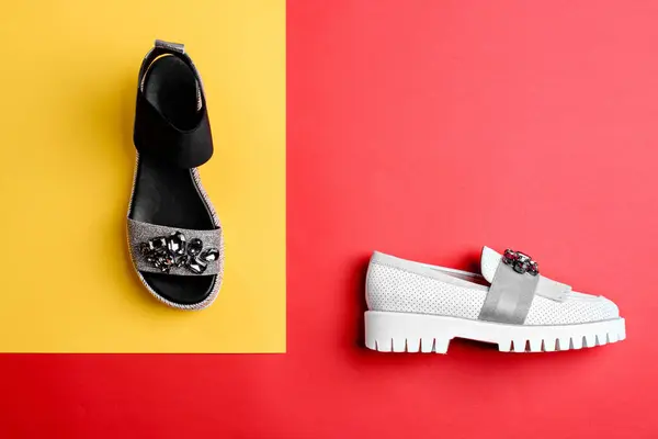 Two different stylish female shoes: white perforated leather loafer whith ribbed sole and black-silver sandal decorated with a scattering of rhinestones on bright contrasting background. Fashion blog.