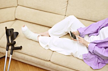 Kırık kadın bacağının yakın plan fotoğrafı. Dirsek değnekleri ve ortopedik alçı. Bacağında beyaz bilek ve ayak bandı var. Genç bir kadının düşme kazası. Yaralanma, travma, iyileşme konsepti. Boşluğu kopyala