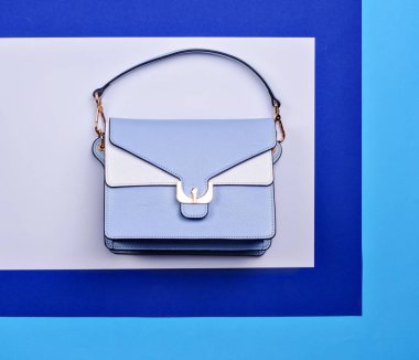 Açık mavi ve beyaz deriden yapılmış, siyah süslemeli zarif bir kadın çantası ve üç tonluk yaratıcı bir arka planda altın toka. Moda blogu ya da dergi konsepti. İndirimli promosyon posteri.